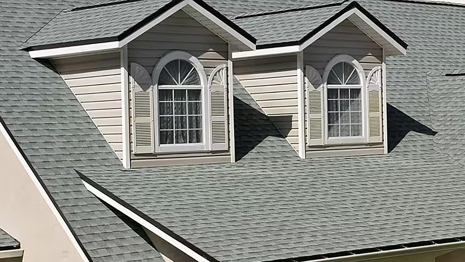 A house roof with two dormer windows featuring arches and white shutters, covered with gray shingles.